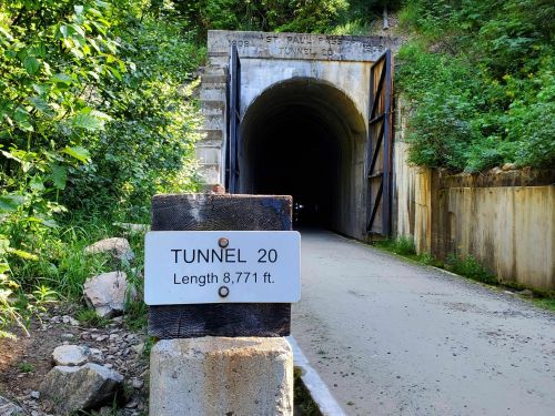 A sign for Tunnel 20, indicating its length of 8,771 feet, with a dark tunnel entrance surrounded by greenery.