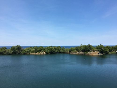 A serene landscape featuring a calm blue lake surrounded by lush greenery under a clear blue sky.