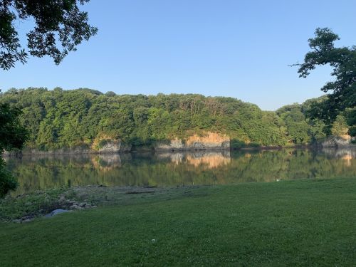 A serene lake surrounded by lush green trees, reflecting the landscape on a clear blue sky day.