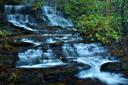 A serene waterfall cascading over rocky steps, surrounded by lush green foliage and misty air.