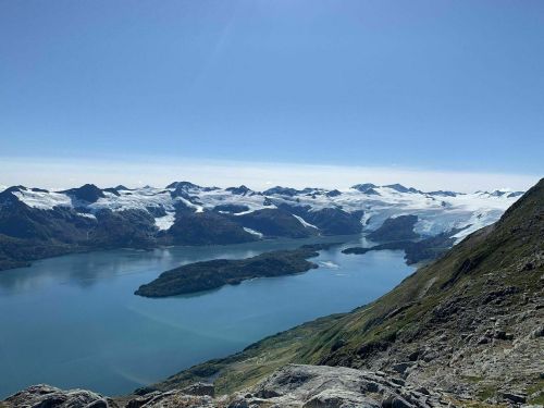 A panoramic view of snow-capped mountains and a serene blue lake under a clear sky.
