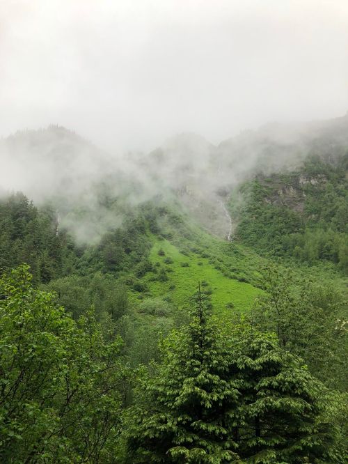 Foggy mountains covered in lush greenery, with waterfalls cascading down the slopes.