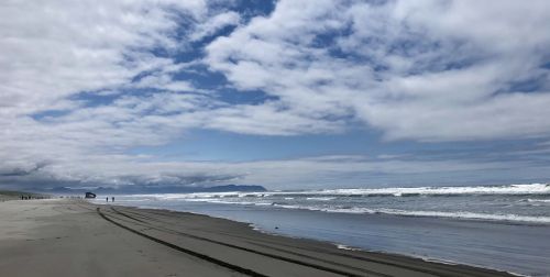 A serene beach scene with gentle waves, cloudy skies, and distant mountains under a blue horizon.