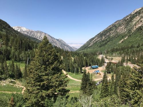 A scenic view of a mountainous landscape with lush green trees, a clear blue sky, and a small area of buildings below.