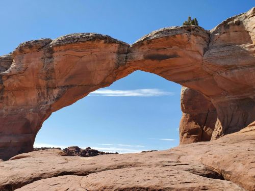 Natural rock arch against a clear blue sky, framed by rugged red rock formations.