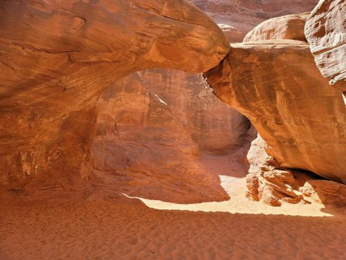 A natural sandstone arch in a desert canyon, with warm orange hues and soft sand below.