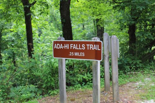 Sign for Ada-Hi Falls Trail, indicating a distance of 0.25 miles, surrounded by lush green trees.