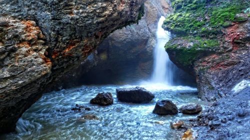 A serene waterfall cascades between rocky cliffs, surrounded by lush greenery and flowing water.