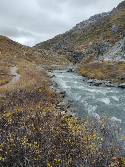 A winding river flows through a rocky landscape with autumn foliage and mountains under a cloudy sky.