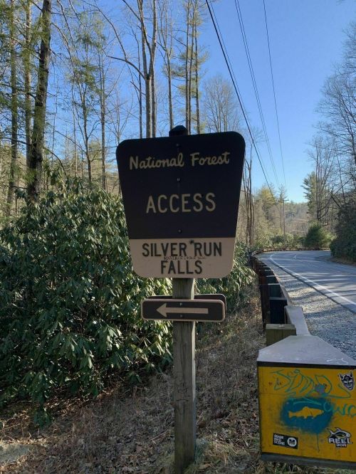 Sign for Silver Run Falls access in a national forest, with a left arrow, surrounded by trees and a clear blue sky.