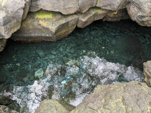 Clear water reflecting light, surrounded by dark, rugged rocks in a natural pool.