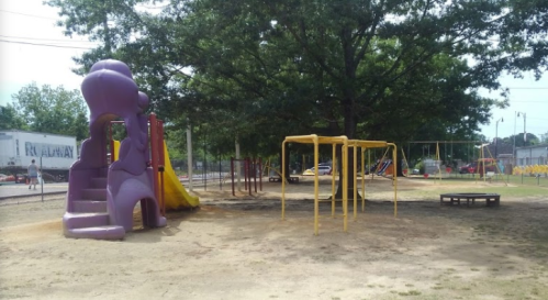 A playground featuring a purple slide, climbing structure, swings, and a large tree in a grassy area.