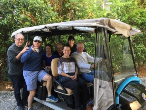 A group of seven people smiling and posing together in a golf cart surrounded by greenery.