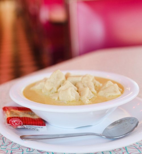 A bowl of dumplings in a creamy sauce, served with a spoon and a packet of sauce on the side.