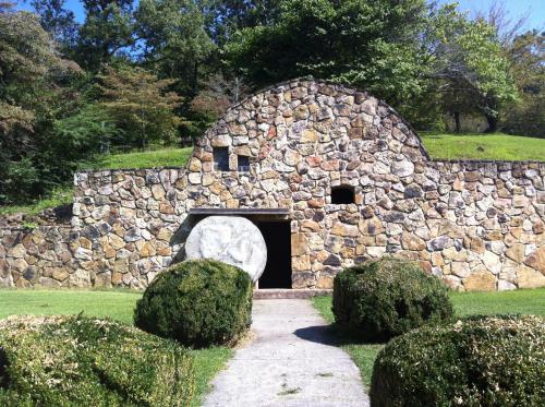 A stone building with a rounded roof, surrounded by greenery and a pathway leading to its entrance.