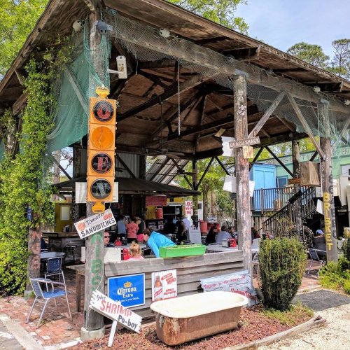 A rustic outdoor eatery with colorful signs, seating, and a lively atmosphere surrounded by greenery.
