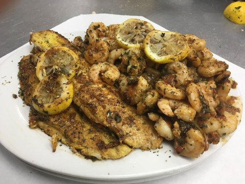 A plate of seasoned fish fillets and shrimp, garnished with lemon slices and herbs.