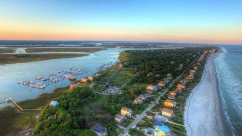 Aerial view of a coastal area with a marina, lush greenery, and a sandy beach under a colorful sunset sky.