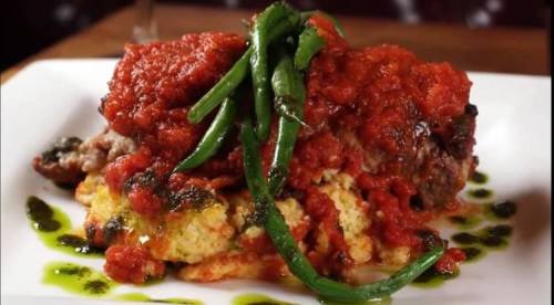 A plate of meat topped with marinara sauce, served on a bed of polenta and garnished with green beans.