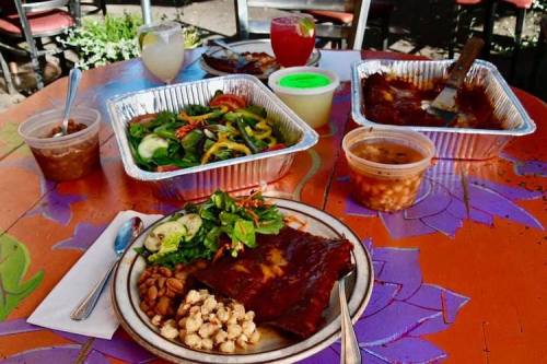 A colorful outdoor table set with plates of enchiladas, salad, beans, and drinks in vibrant containers.