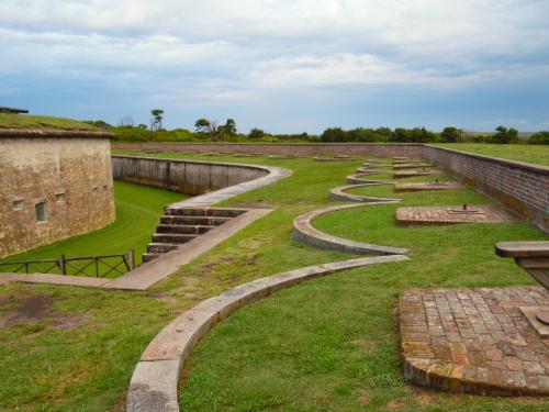 A historic fort with grassy grounds and curved pathways under a cloudy sky.