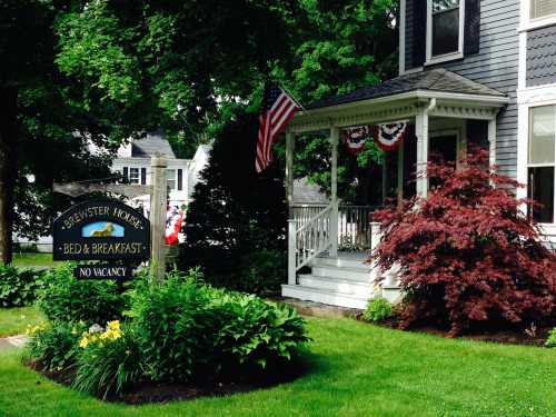 A charming bed and breakfast with a porch, American flag, and colorful flowers in a lush green garden.