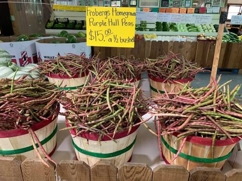 Baskets of purple hull peas for sale, priced at $15 per half bushel, in a market setting.