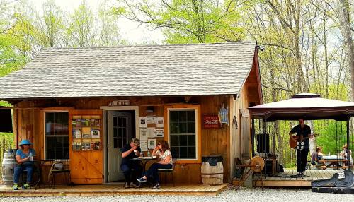 A rustic wooden building with a sign reading "Antiques," featuring outdoor seating and a musician performing nearby.