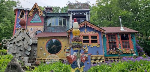 Colorful, whimsical house with unique architecture and vibrant decorations, surrounded by greenery and flowers.