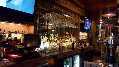 A well-stocked bar with various bottles, glasses hanging above, and multiple screens displaying sports.