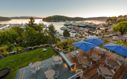 Scenic view of a marina at sunset, featuring boats, trees, and outdoor seating with blue umbrellas.