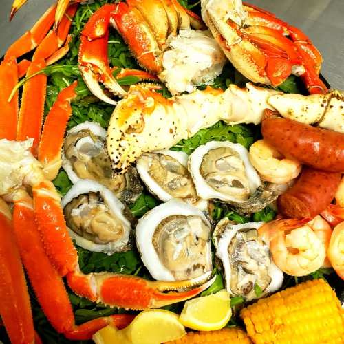 A vibrant seafood platter featuring crab, lobster, oysters, shrimp, sausage, and corn on a bed of greens.