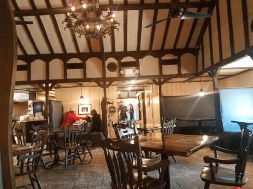 Cozy restaurant interior with wooden beams, tables, and patrons enjoying their meals in a warm atmosphere.