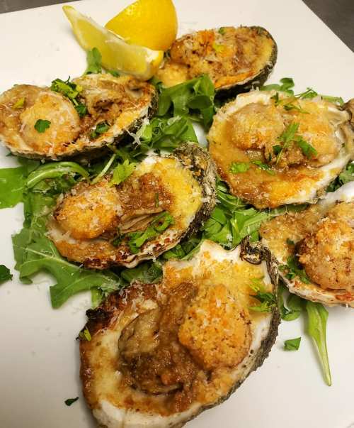 A plate of baked oysters topped with breadcrumbs and shrimp, garnished with fresh greens and a lemon wedge.