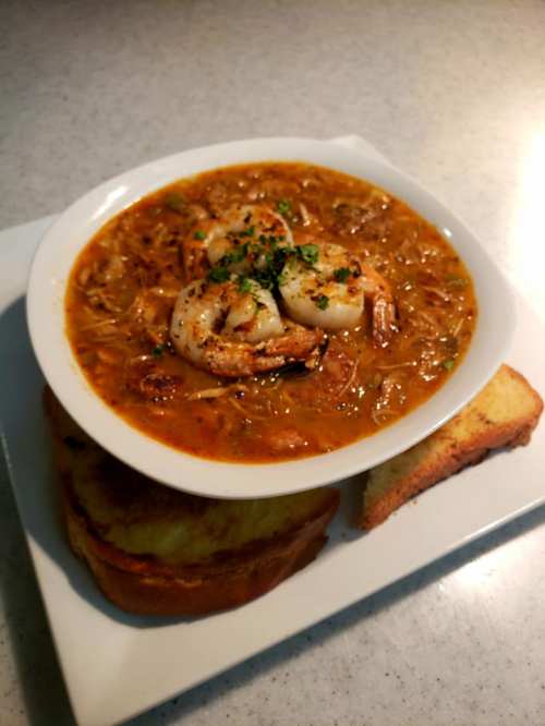 A bowl of shrimp gumbo garnished with herbs, served with slices of toasted bread on a white plate.