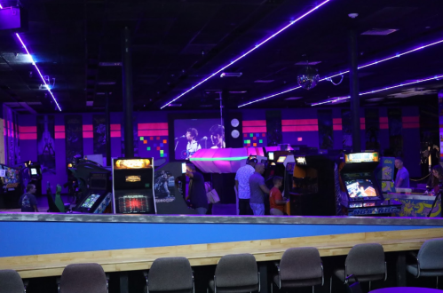 A vibrant arcade with neon lights, featuring vintage games and a crowd enjoying the atmosphere.