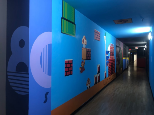 Colorful mural depicting 80s video game characters and elements on a hallway wall, with blue and vibrant graphics.