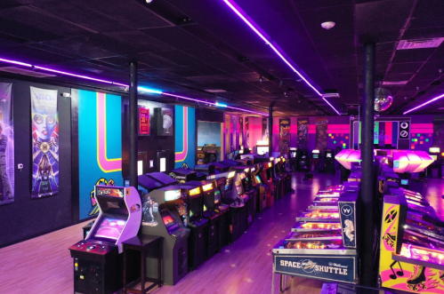 A vibrant arcade filled with classic arcade machines and pinball games, illuminated by colorful neon lights.