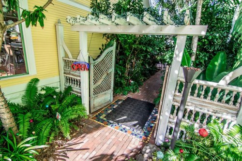 A welcoming entrance with an "OPEN" sign, surrounded by lush greenery and a colorful tiled pathway.