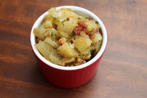 A small red bowl filled with seasoned diced potatoes and herbs on a wooden surface.