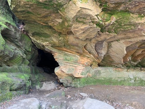 A rocky cave entrance with textured walls and moss, leading into a dark interior.
