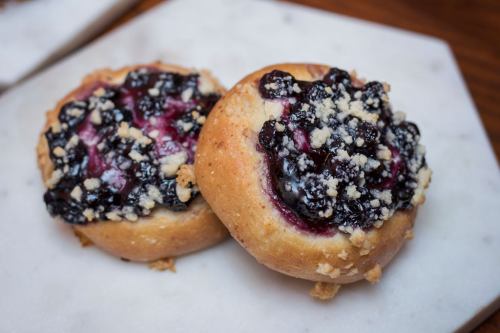 Two sweet pastries topped with blueberry filling and crumbly streusel on a marble surface.