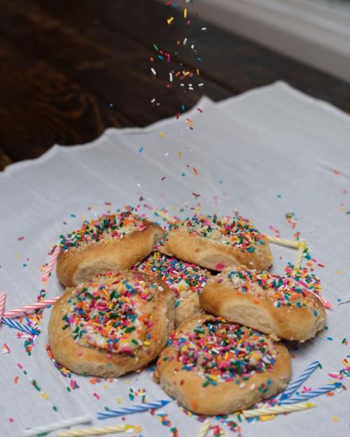A pile of cookies topped with colorful sprinkles, surrounded by scattered sprinkles and birthday candles on a white cloth.