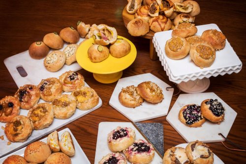 A variety of baked goods displayed on marble and wooden surfaces, including rolls and sweet pastries.