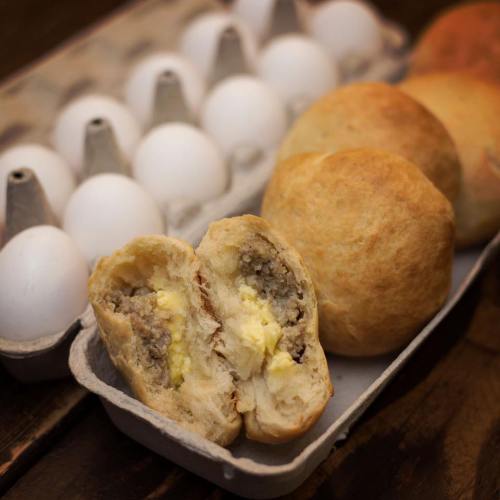 A close-up of a split bread roll filled with meat and egg, alongside a carton of white eggs.