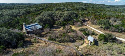 Aerial view of a rustic building surrounded by lush greenery and a winding path in a natural landscape.