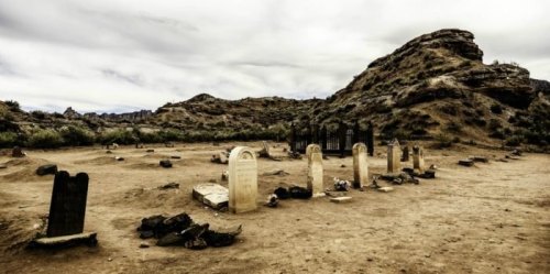 A desolate graveyard with weathered tombstones, surrounded by rocky hills under a cloudy sky.