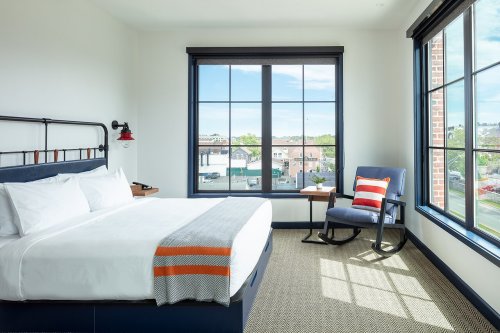Bright hotel room with a large window, featuring a bed, rocking chair, and a view of the outdoors.