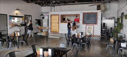 A cozy restaurant interior with a food truck counter, tables, and a staff member serving customers.
