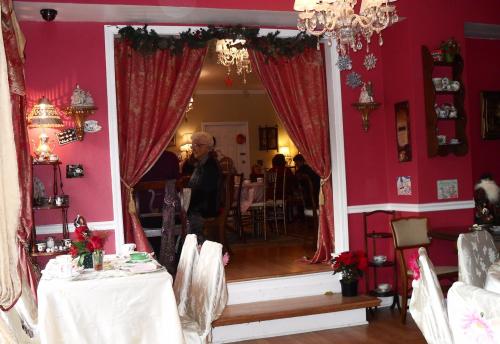 A cozy tea room with pink walls, festive decorations, and guests enjoying tea at elegantly set tables.